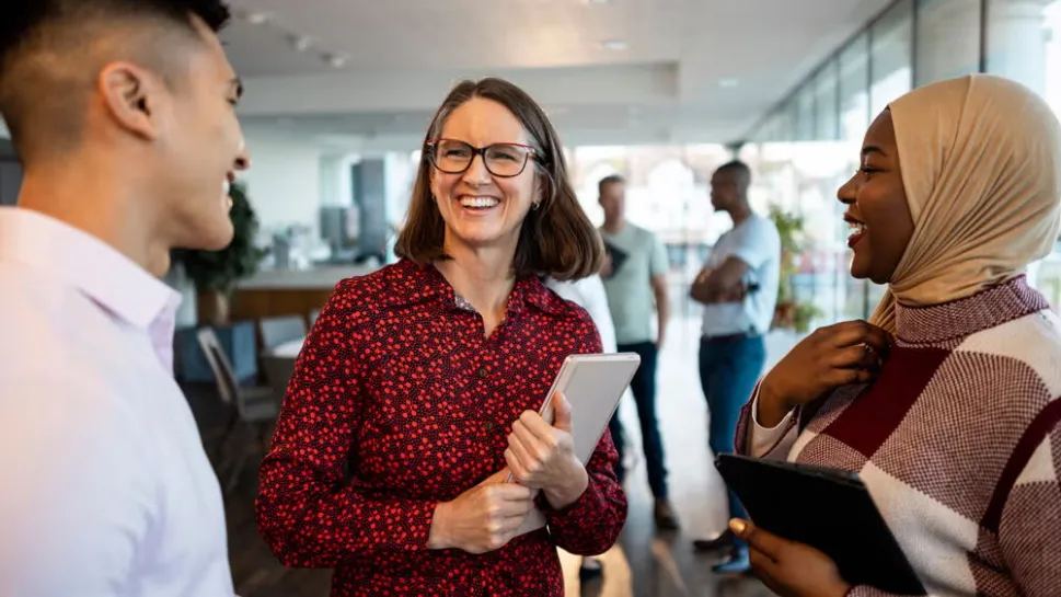 Three diverse colleagues laugh and connect in an office hallway, representing what social workers do day to day