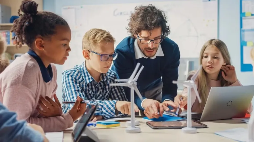 A teacher and students gather around wind turbines in a classroom, illustrating why STEM is important in education careers