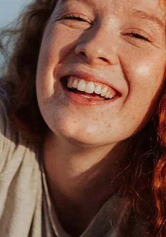 A woman with red hair smiles warmly at the camera, exuding a cheerful and friendly demeanor.