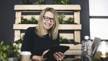 A smiling professional woman holds a tablet in a modern workspace, representing top productivity apps for working students