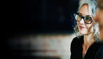1. A woman and a man, both wearing glasses, are smiling and engaged in conversation.